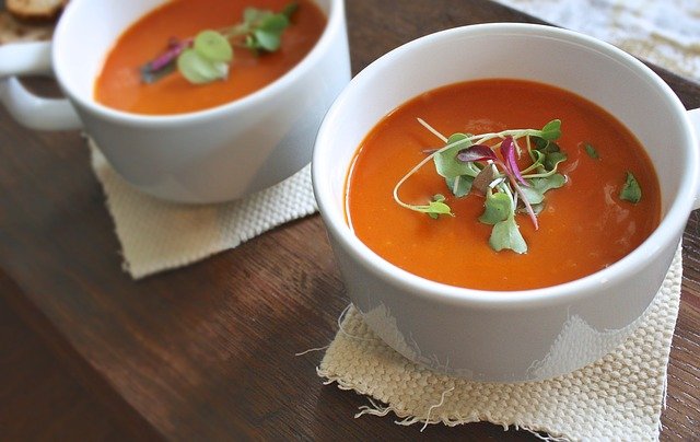 Deux soupes de potimarron dans des bols blancs présentés avec des herbes pour la décoration